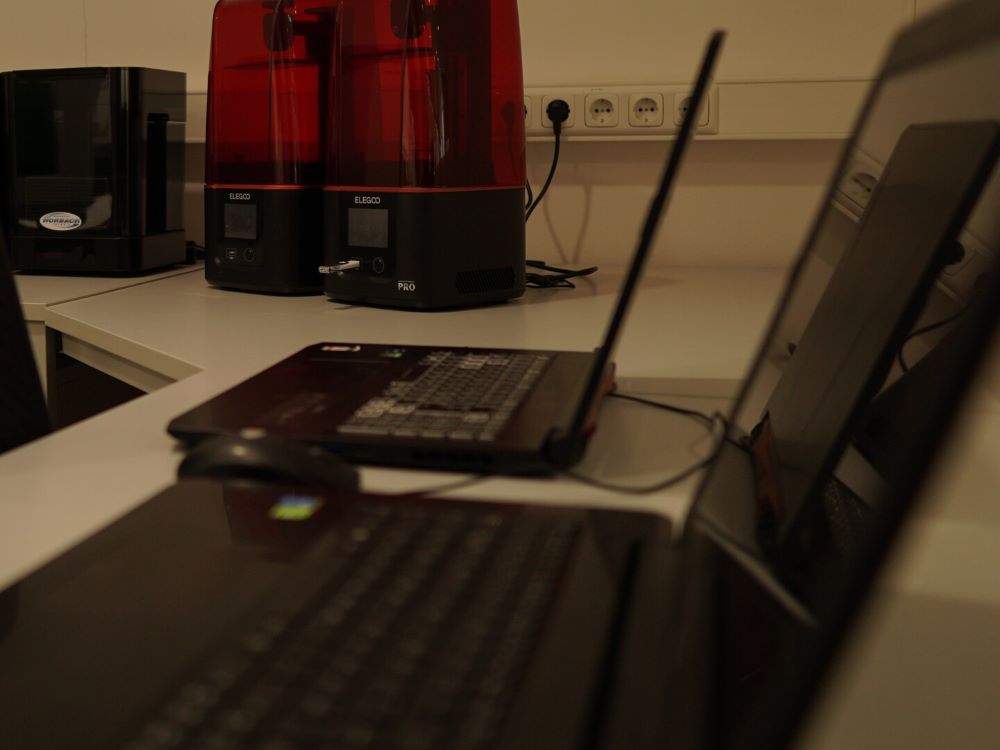 Ein geöffneter Laptop, im Hintergrund 3D-Drucker