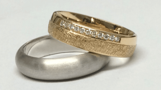 Ein stark gerundeter Palladium-Ring, dazu ein gelbgoldener Ring mit Steinreihe.