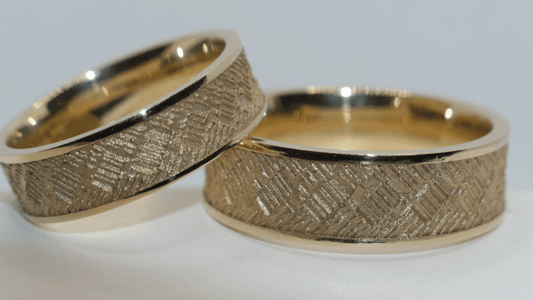 Ein gelbgoldenes Trauringpaar mit schmalen Rändern und einer über Kreuz geritzten Oberfläche.